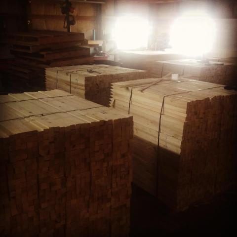 Pallets of milled hardwood stakes inside the Basic Industries shop, sunlight pouring through the windows.